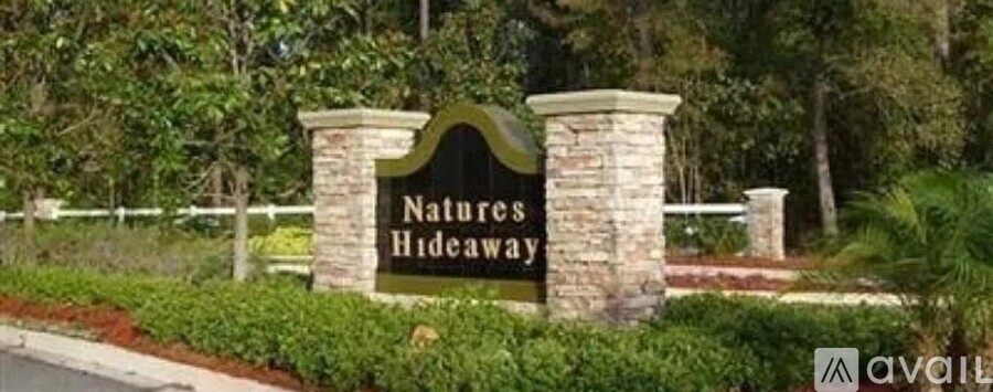A sign that says "Natures Hideaway" is in front of a fence.
