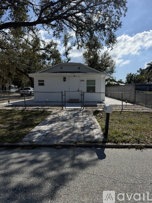 A small white building with a gabled roof is surrounded by a fence and trees.