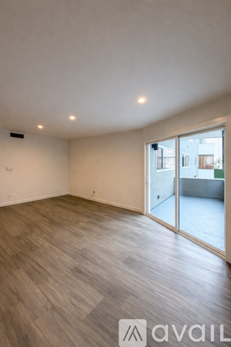 A spacious room with wooden flooring and a sliding glass door.
