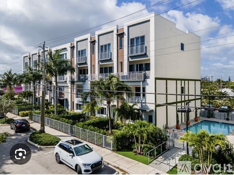 A white car is parked in front of a building with a pool.