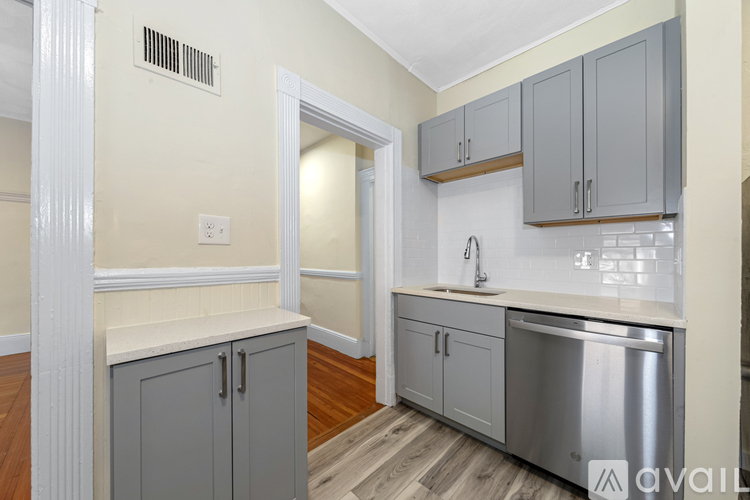 A kitchen with a stainless steel dishwasher and grey cabinets.