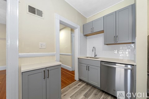 A kitchen with a stainless steel dishwasher and grey cabinets.