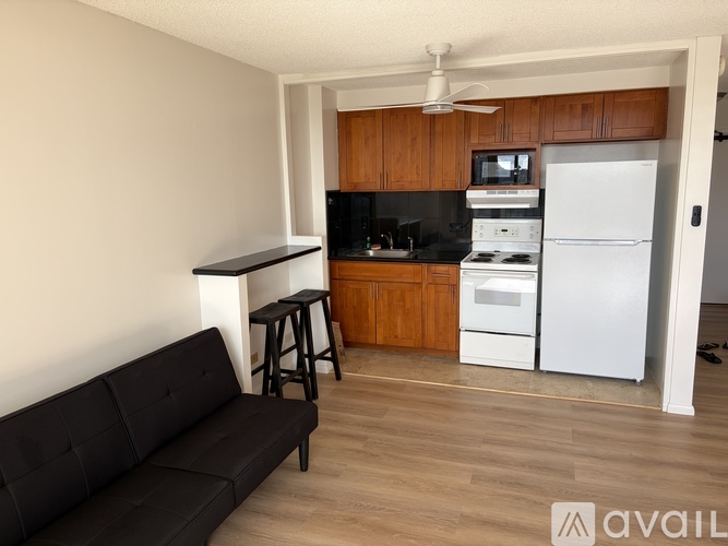 A black couch sits in a kitchen with a white refrigerator.