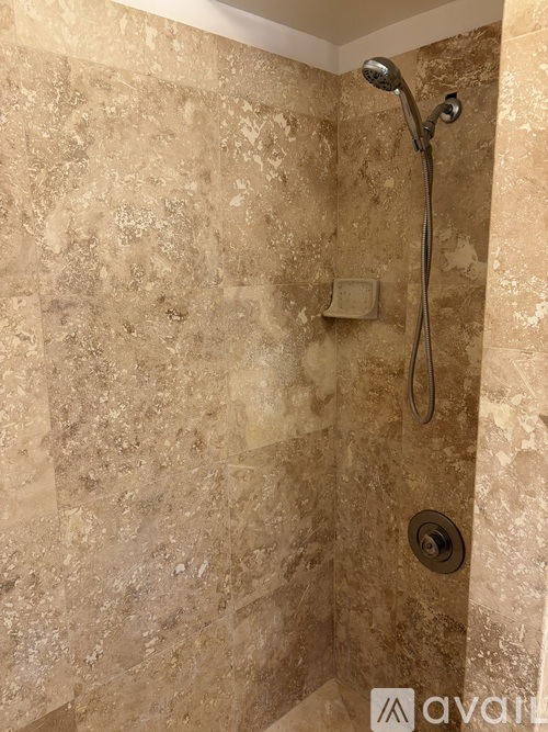 A shower with a gold tile wall and a gold shower head.