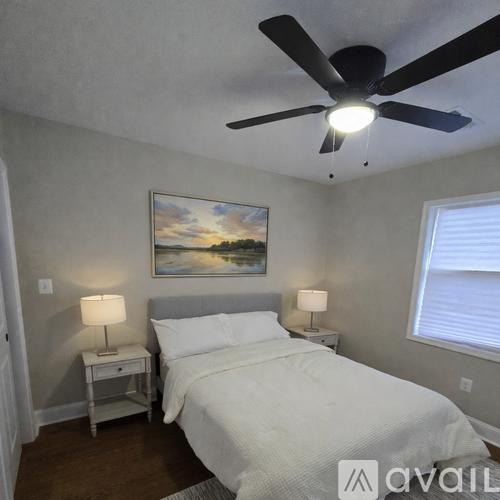 A bedroom with a bed, two lamps, and a painting on the wall.