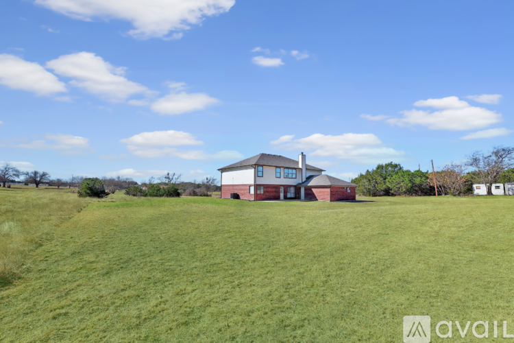 A house with a red brick exterior is situated in a grassy field.