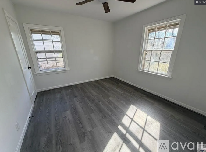 A room with wooden flooring and two windows.