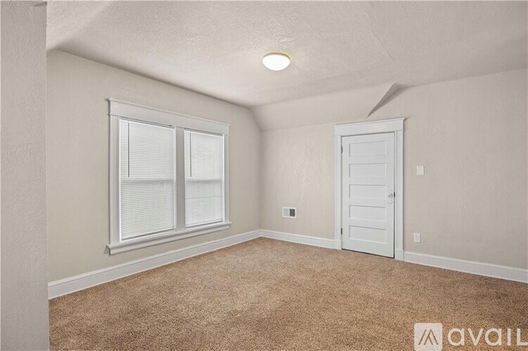 A room with a carpeted floor, a window with blinds, and a white door.