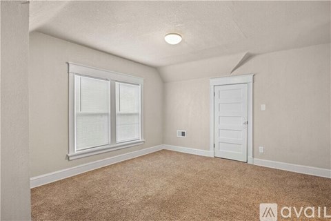 A room with a carpeted floor, a window with blinds, and a white door.