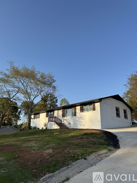 A house with a white exterior and a brown roof is surrounded by grass and trees.