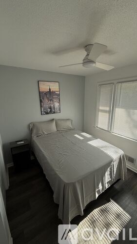 A bedroom with a bed, a ceiling fan, and a picture on the wall.