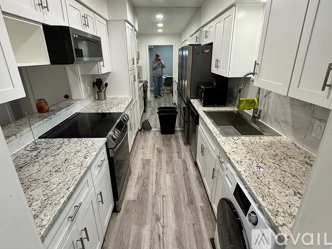 A man is standing in a kitchen with white cabinets and granite countertops.