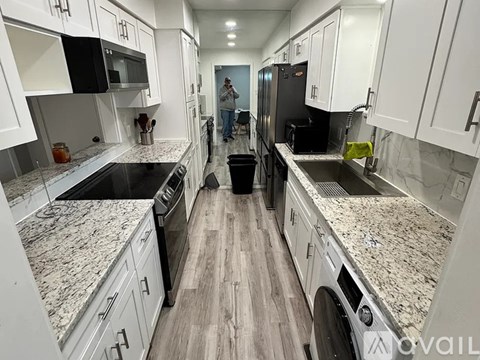 A man is standing in a kitchen with white cabinets and granite countertops.