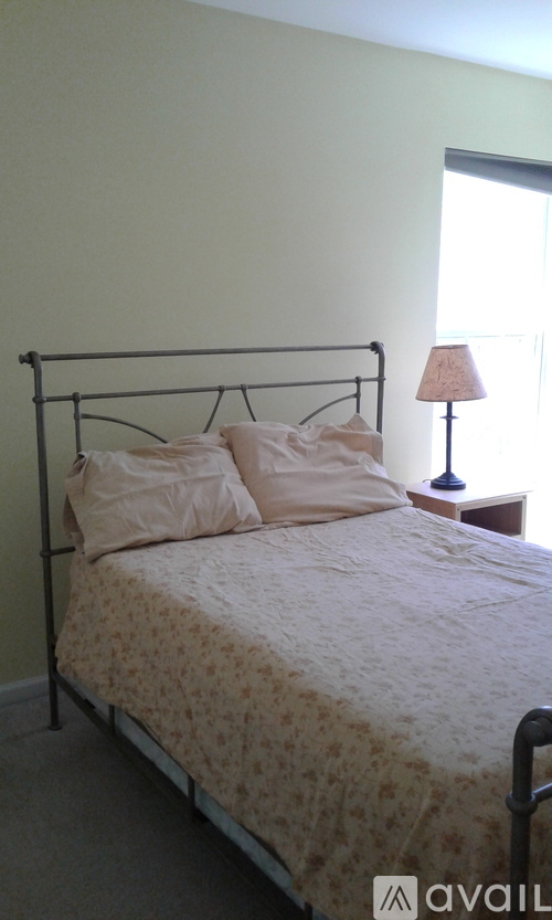 A bed with a floral patterned bedspread and two pillows sits in a room with a lamp on a side table.