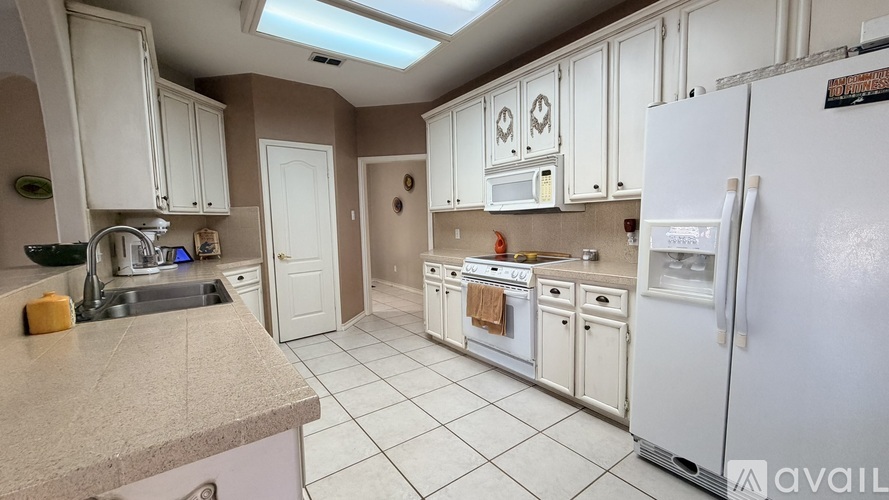 A kitchen with white cabinets and appliances, a skylight, and a countertop with a yellow object on it.