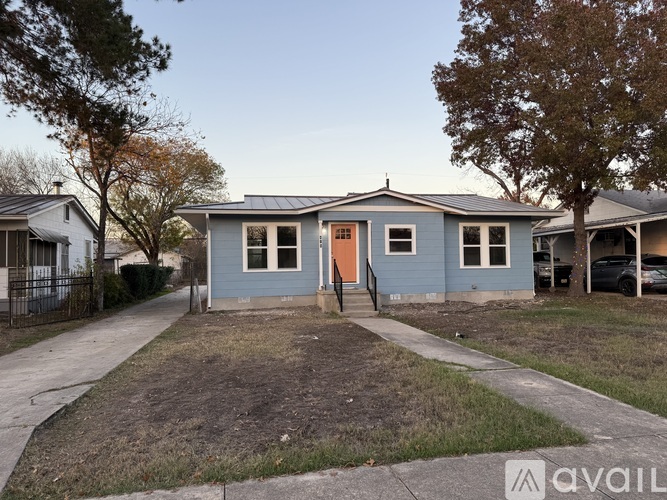 A blue house with a brown door is in the foreground with a tree to the left and a car to the right.