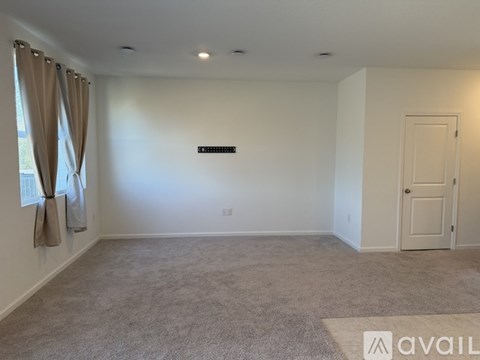 A spacious room with a carpeted floor, a door, and a window with curtains.