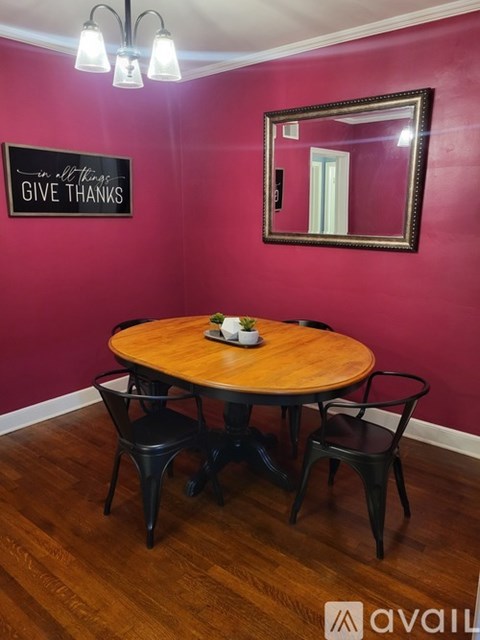 A round wooden table with four chairs in front of a pink wall with a mirror and a sign that says "Give Thanks".