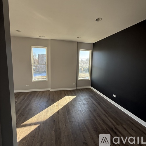 A spacious room with wooden floors and two windows.