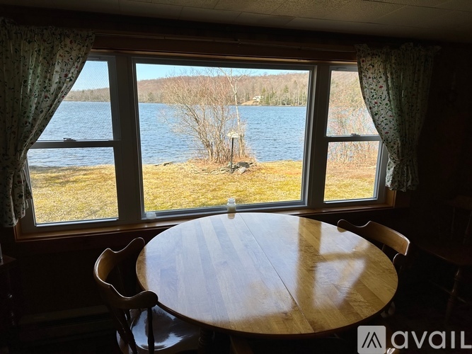 A round wooden table is in front of a window with a view of a lake and trees.