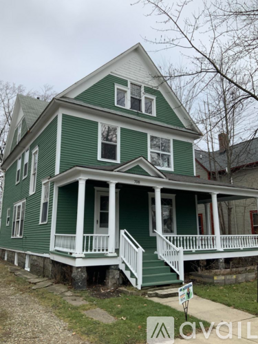 A green house with a porch and a sign in front.