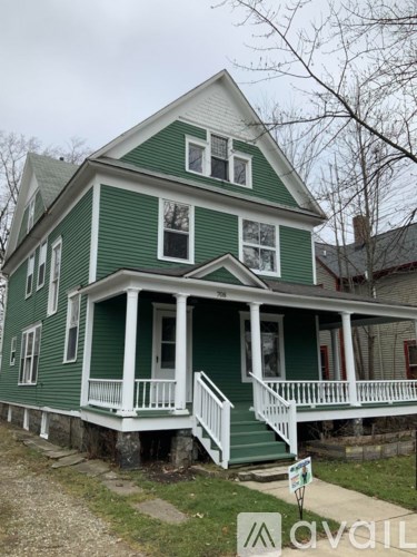 A green house with a porch and a sign in front.