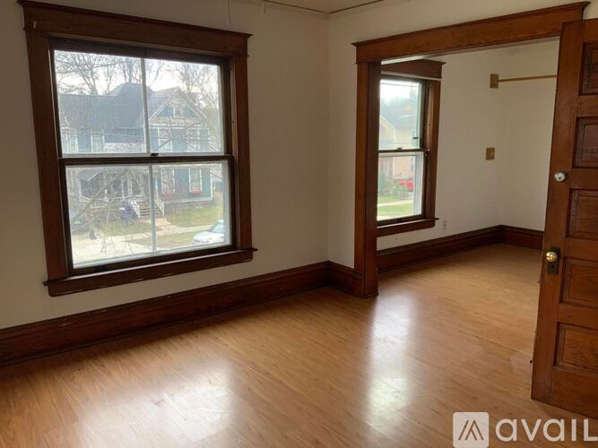 A room with wooden floors and a large window with a view of a backyard.