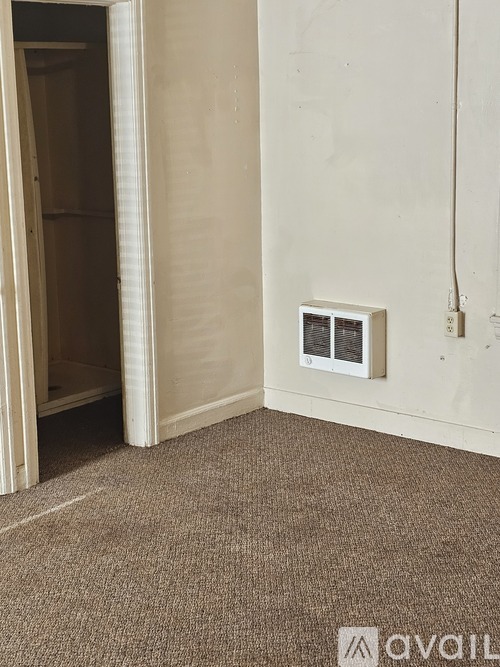 A room with a carpeted floor and a wall-mounted electrical outlet.