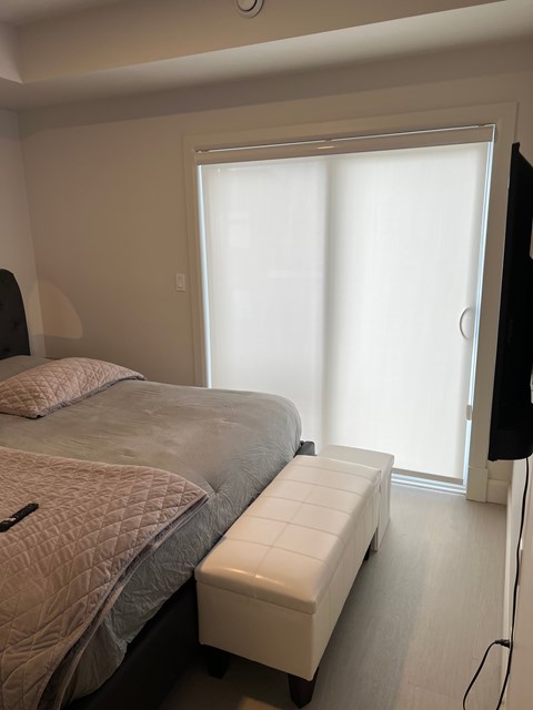 A bedroom with a bed, a bench, and a window with blinds.