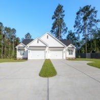 A white house with a grey roof and a driveway in front.
