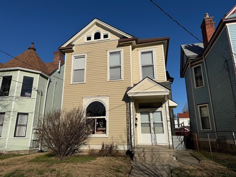 A two-story house with a front porch and a small tree in front.