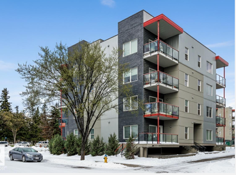 A grey apartment building with red accents stands in the snow.