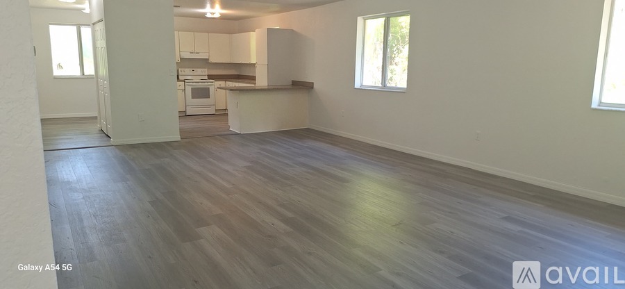 A spacious room with wood flooring and a kitchen area in the background.