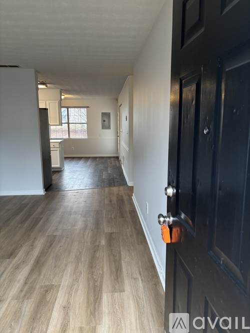 A hallway with a black door and wooden flooring.