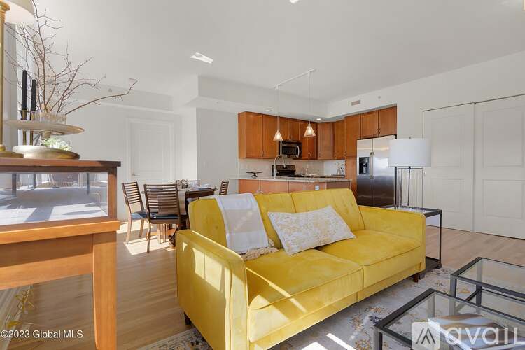 A yellow couch sits in a brightly lit living room with a glass coffee table in front of it.