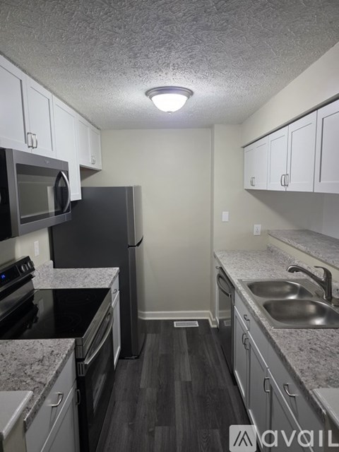 A kitchen with a black refrigerator, black countertops, and white cabinets.