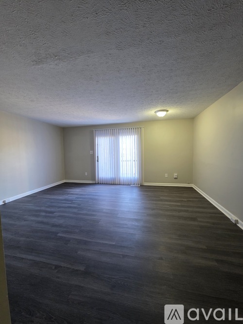 A room with a window covered by white curtains and a wooden floor.