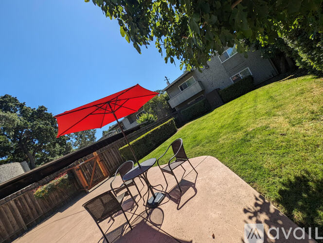 A backyard with a table and chairs under a red umbrella.