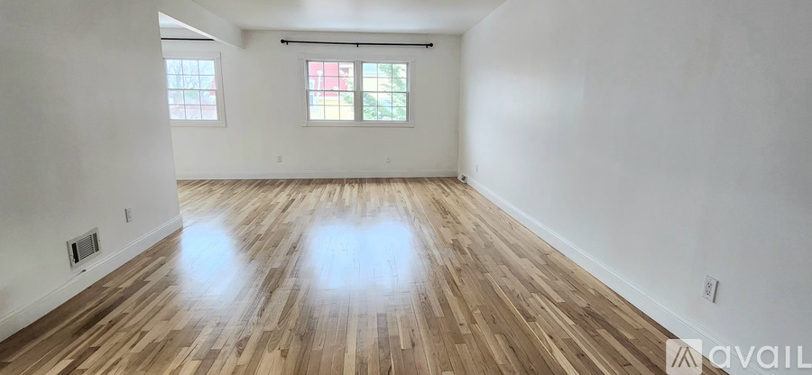 A room with wooden flooring and two windows.