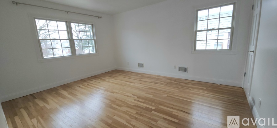 A room with wooden flooring and two windows.