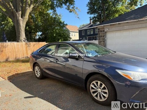 A blue car is parked in front of a wooden fence and a house.