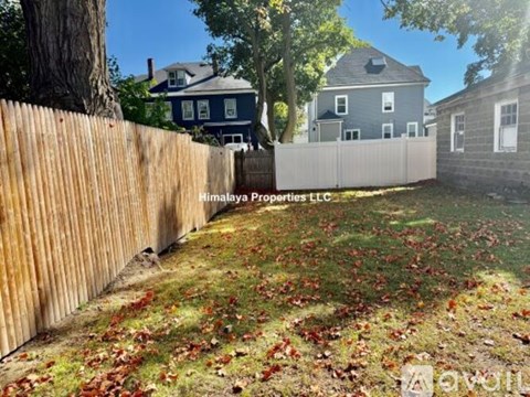 A wooden fence with leaves on the ground in front of a house.