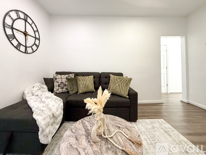 A living room with a black couch and a clock on the wall.