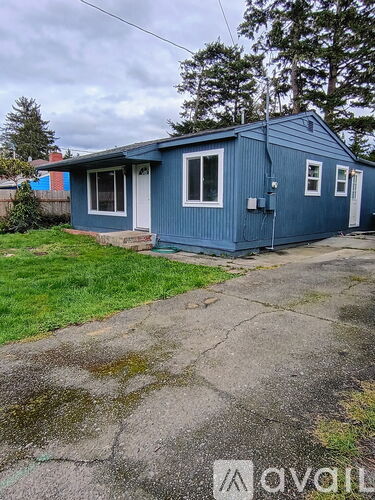A blue house with a white door and windows is surrounded by grass and a concrete driveway.