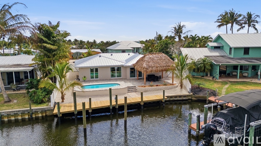 A house with a thatched roof is situated on a dock with a swimming pool.
