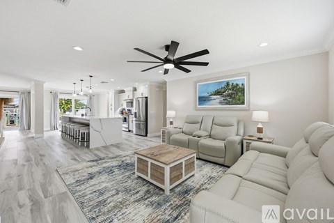 A spacious living room with a white ceiling fan and a painting of a beach scene on the wall.