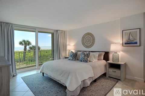 A bedroom with a large bed and a view of the ocean through the sliding glass doors.