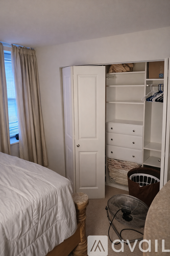 A bedroom with a white bed and a white wardrobe with clothes inside.
