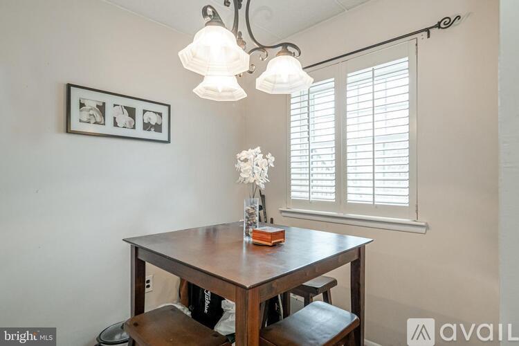 A dining room with a wooden table and chairs, a vase with flowers, and a framed picture on the wall.