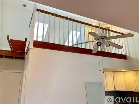 A white ceiling fan hangs from a wooden beam in a room with white walls.
